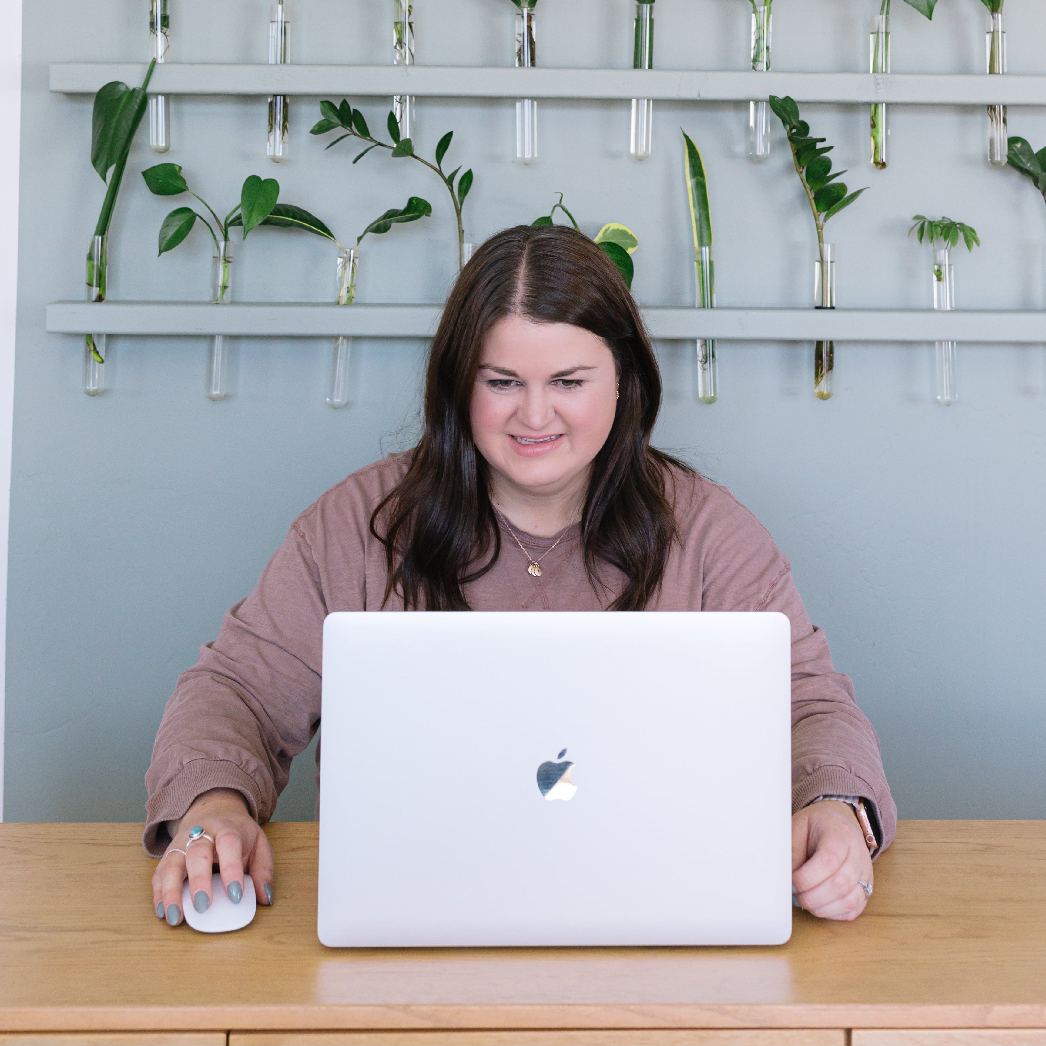 Person sitting at a desk with a laptop in front of a wall with plants